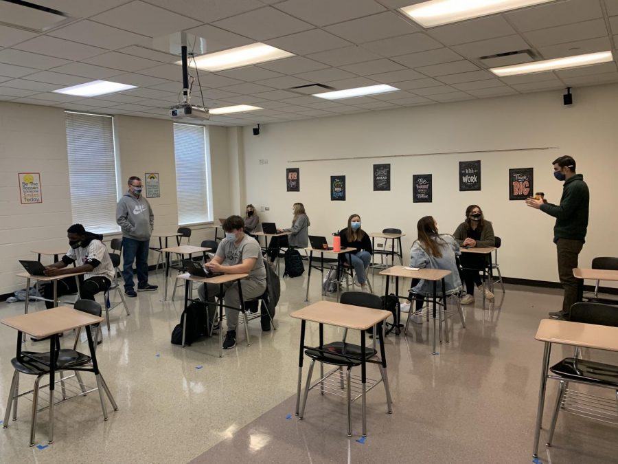 Students in broadcasting class sit six feet apart to work on their broadcasts while their classmates work with them on Zoom.